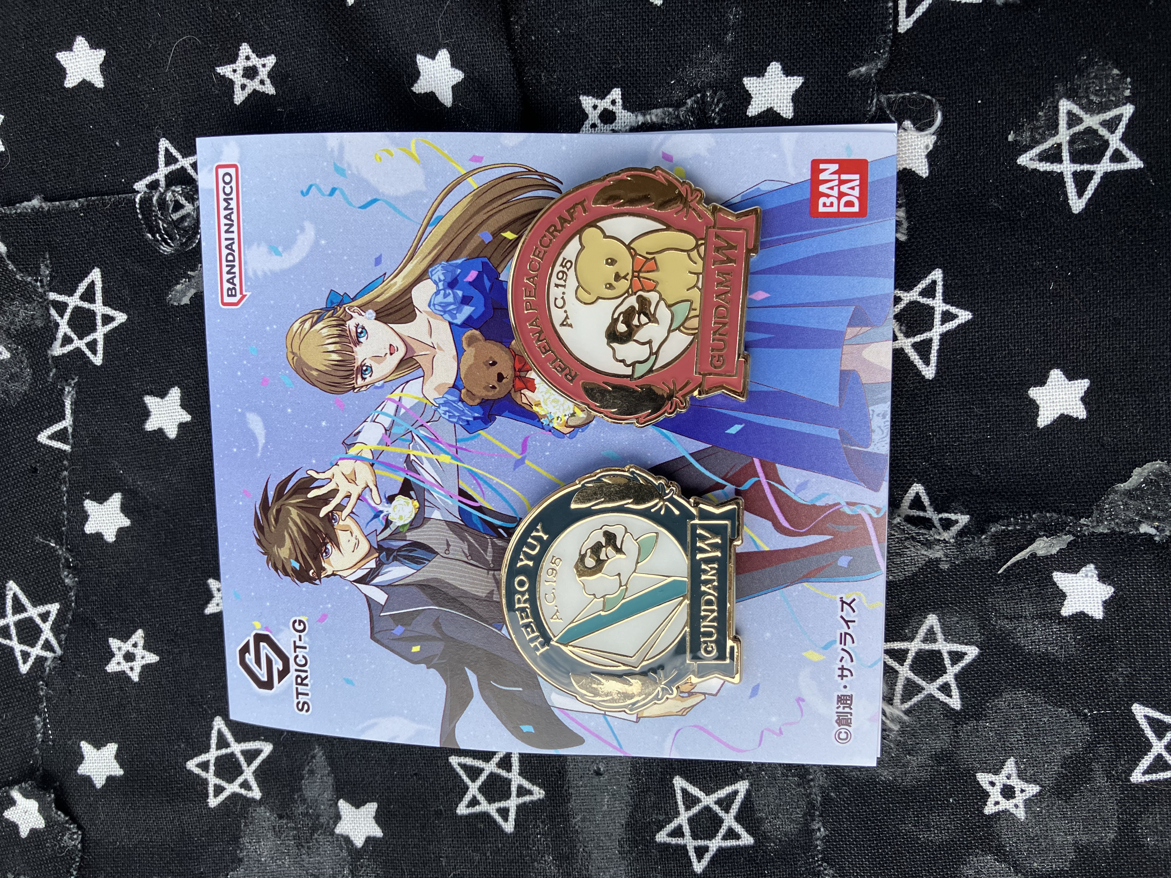 Two collectible enamel pins with Gundam wing Relena and Heero in formal attire as the backing card. The Heero pin has a white rose and envelope. The Relena pin has a white rose and a teddy bear.